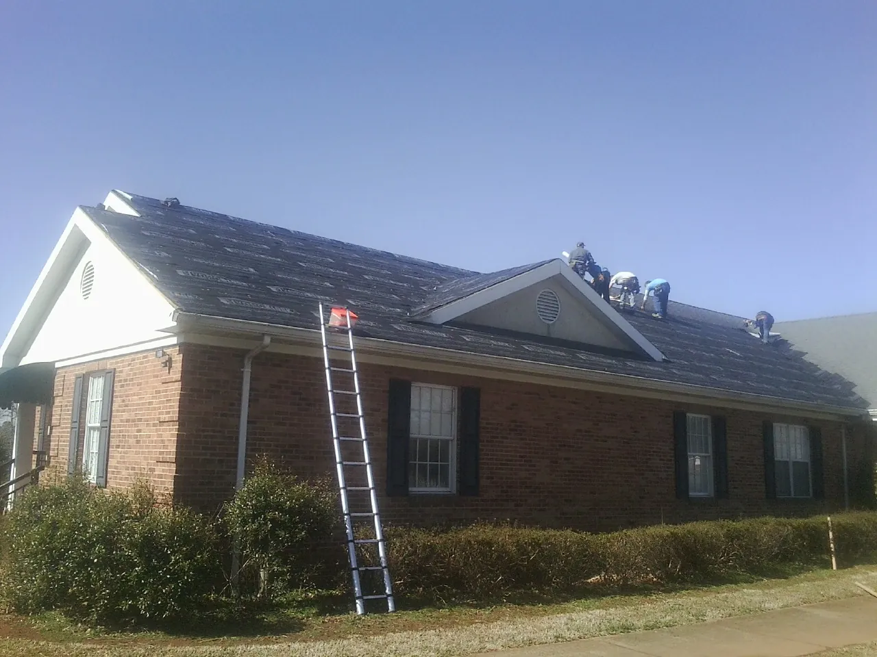 Crew tearing shingles off a brick ranch roof with a ladder set — Emergency Roof Repair work by our crew in Mount Holly