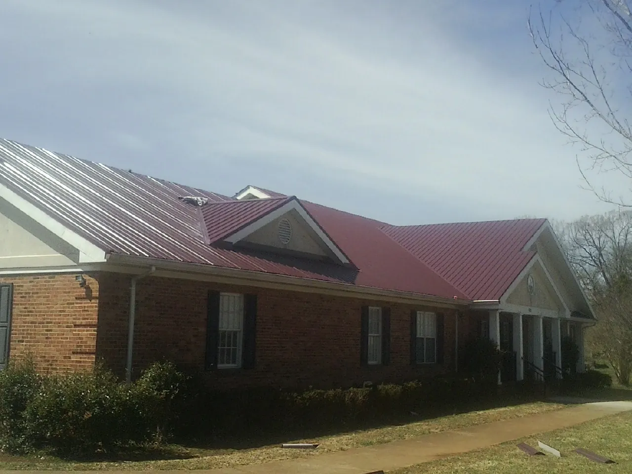 Red metal roof with gabled entries on a long brick building, from a Hail Damage Roof Repair job in Mount Holly