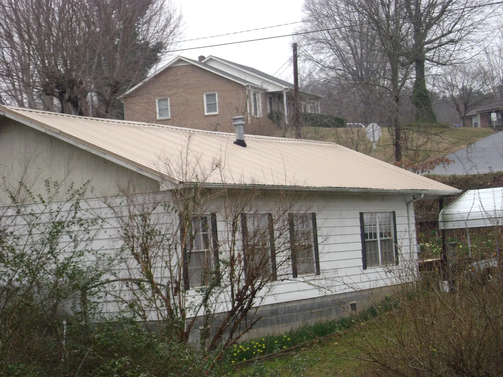 Tan metal roof on a white sided house set into a hillside — Commercial Roofing by Roofing Brothers in Mount Holly